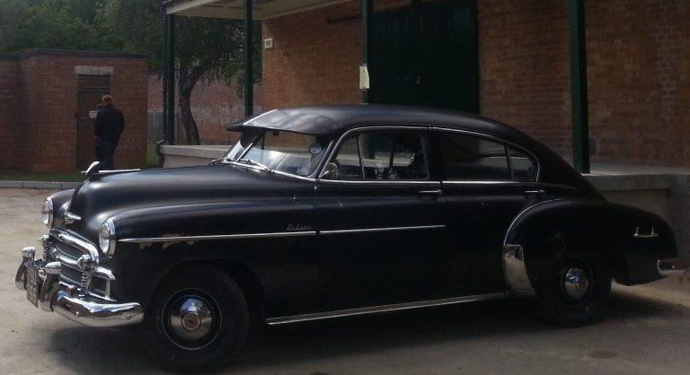 A picture of a black 1950 chevrolet ouside a brick and concrete building